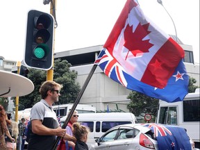 Ein Demonstrant steht mit neuseeländischen und kanadischen Flaggen in der Nähe des Parlamentsgebäudes in Wellington am 8. Februar 2022 während einer Demonstration gegen COVID-Beschränkungen, inspiriert von einer ähnlichen Demonstration in Kanada.