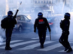 Ein französischer Anti-Riot-Polizist feuert am 12. Februar 2022 einen Tränengaskanister auf den Champs Elysees in Paris als sogenannte Konvois von Demonstranten ab 