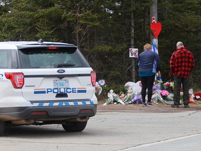 Mourners pay their respects in front of the makeshift memorial, made in the memory for the victims of Sunday’s mass shooting as a RCMP vehicle passes nearby in Portapique, N.S., April 23, 2020.