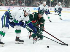 Nic Petan of the Vancouver Canucks and Tyson Jost of the Minnesota Wild vie for the puck in the first period at Xcel Energy Center on March 24, 2022 in St Paul, Minnesota.