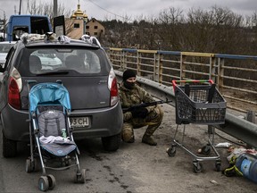 A Ukrainian serviceman takes cover behind a car in the city of Irpin, northwest of Kyiv, on March 13, 2022.