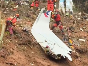 This screengrab taken on March 24, 2022 from video by state broadcaster China Central Television (CCTV) via AFPTV shows rescue teams with a piece of the fuselage as they continue their search at the site of where a China Eastern passenger jet crashed onto a mountainside near Wuzhou City in China's southern Guangxi region.