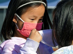 Tessa Ng (left, 5) helps her friend Liv Leong (5) put on a face mask during the COVID-19 pandemic in Edmonton. On November 19, 2021