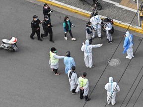 A health worker (centre) wearing personal protective gear gestures to residents on a street during the second stage of a COVID-19 lockdown in Jing'an district in Shanghai on April 1, 2022.