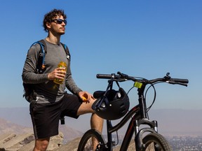 Young biker holding water bottle next to mountain bike