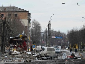 People walk among debris of destroyed cars and damaged buildings on a street in the town of Borodianka, northwest of Kyiv, Wednesday, April 6, 2022, during Russia's military invasion of Ukraine.