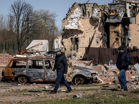 Männer gehen am Donnerstag, den 14. April 2022, inmitten der russischen Invasion in der Ukraine in der Nähe eines verbrannten Autos und eines beschädigten Hauses im Dorf Bohdanivka nordöstlich von Kiew vorbei.