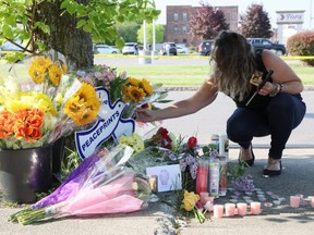 A mourner crouches by flowers and candles, during a vigil for victims of the shooting at a TOPS supermarket in Buffalo, N.Y., Sunday, May 15, 2022.