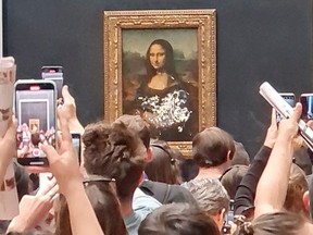 Visitors take pictures and video of the painting "Mona Lisa" after cake was smeared on the protective glass at the Lourve Museum in Paris, France May 29, 2022 in this screen grab obtained from a social media video. Twitter/@klevisl007/via REUTERS