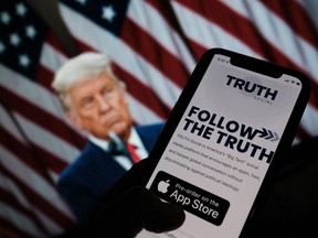 This illustration photo shows a person checking the app store on a smartphone for "Truth Social", with a photo of former president Donald Trump on a computer screen in the background, in Los Angeles, Oct. 20, 2021.