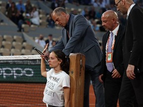 Security personnel use bolt cutters to release an activist (C) after she attached herself to the tennis net during the men's semi-final singles match between Norway's Casper Ruud and Croatia's Marin Cilic on day thirteen of the Roland-Garros Open tennis tournament at the Court Philippe-Chatrier in Paris on June 3, 2022.