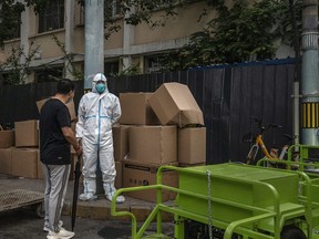 Ein Gesundheitspersonal trägt einen Schutzanzug, während er neben Kisten mit Abfall steht, der entfernt werden soll, während er mit einem Passanten neben der Sperrwand einer Wohnung spricht, die nach einem kürzlichen COVID-19-Ausbruch am 11. Juni 2022 in Peking gesperrt wurde.