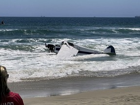 A small plane sits in the surf after it crashed into the ocean just off Huntington Beach, Calif. on Friday, July 22, 2022, during a lifeguarding competition.