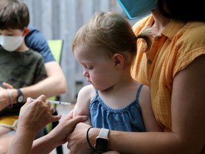 Two-year-old Beatrice Giles warily watches the needle as she sits on her mom Kristina Pawk's lap while getting her vaccine. Her older brother Theo Giles, 4 (rear) also got his at the event. Dr. Nili Kaplan-Myrth held a "Jabapalooza" mass COVID vaccination event in the parking lot behind her doctor's office in the Glebe Thursday. Julie Oliver/Postmedia