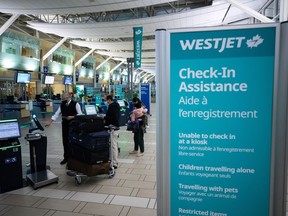 A Westjet employee assists people checking in for a domestic flight at Vancouver International Airport, in Richmond, B.C., on Thursday, Jan. 21, 2021.