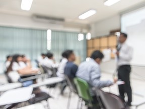 Blurred abstract background of students sitting in classroom with teacher in front of class.