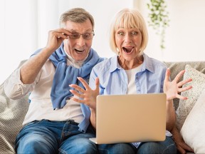 Surprised, happy mature couple looking at winning lottery numbers on laptop