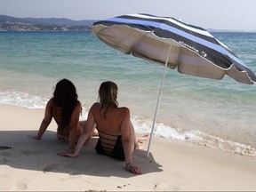 In this file photo, women sit under the shade of an umbrella on Ricanto beach in Ajaccio, on the French Mediterranean island of Corsica, on Aug. 1, 2017
