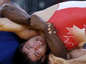 Khetag Pliev of Canada, (in red) and Javier Cortina Lacerra of Cuba, (in blue) compete during their 66-kg freestyle wrestling match at the 2012 Summer Olympics, Sunday, Aug. 12, 2012, in London.
