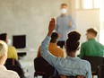 Back view of black female student raising arm to ask a question during a lecture in the classroom.