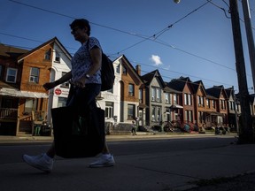 A person walks by a row of houses in Toronto, July 12, 2022. The federal government's newly announced inflation relief for low-income Canadians through the goods and services tax rebate stacks up as better policy than some of the cash payments issued by provinces, economists say.