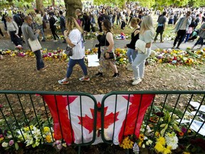 Lange Reihen von Trauernden bilden sich und legen Blumen in der Nähe einer kanadischen Flagge nieder, während die Menschen darauf warten, am Sonntag, den 11. September 2022, vor den Toren des Buckingham Palace in London ihren Respekt zu erweisen.