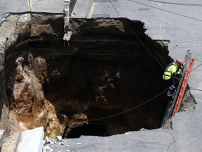 A rescuer walks down a ladder into a giant hole in a road, in Villa Nueva, on September 25, 2022.