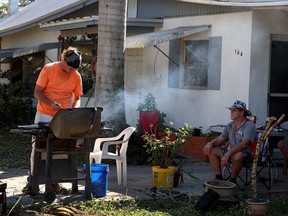 Dean T. Davis 3rd, (left) and Dean T. Davis Jr. cook outdoors since their house has no electricity on October 7, 2022 in Fort Myers, Florida.