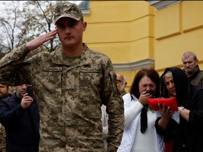 A serviceman salutes as relatives react beside the coffin of Georgian volunteer Edisher Kvaratskhelia after his funeral, amid Russia's attack on Ukraine, outside St. Volodymyr cathedral in Kyiv, Oct. 13, 2022.