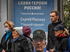 In this file photo, pedestrians walk past a poster displaying a Russian soldier with a slogan reading "Glory to the Heroes of Russia" decorating a bus stop in central Moscow on Oct. 12, 2022.