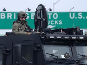 An Ontario Provincial Police tactical officer looks on from the top hatch of an armoured vehicle as demonstrators prepare to leave in advance of police enforcing an injunction against their demonstration, which has blocked traffic across the Ambassador Bridge by protesters against COVID-19 restrictions, in Windsor, Ont., Saturday, Feb. 12, 2022.