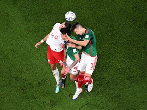 Poland's defender Jakub Kiwior and Mexico's Edson Alvarez (#4) and Cesar Montes jump for a header during their World Cup match.
