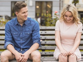 Shy blonde girl smiling, attractive guy flirting with beautiful woman on bench