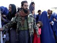 A Taliban fighter stands guard as people receive food rations distributed by a Saudi humanitarian aid group, in Kabul, Afghanistan, Monday, April 25, 2022.