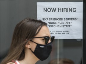 A pedestrian wearing a mask walks past help wanted signage at Queen's Pasta Cafe in Toronto, June 9, 2021.