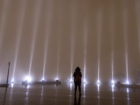 A lone woman braves the rain to take a moment in silence as the sky is lit with 14 beams of white light during ceremonies to mark the anniversary of the massacre at Ecole Polytechnique in Montreal, on Tuesday, Dec. 6, 2022.