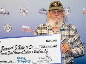 Man with white beard and wearing glasses holding cheque that reads "Twenty five thousand dollars a year for life."