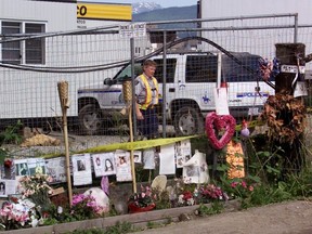 An RCMP officer patrols the entrance to the Port Coquitlam pig farm behind a fence and a memorial to some of the fifty missing women, as the search continues for their remains on the farm Wednesday June 26, 2002.