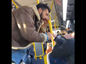 A seated man covers his head as a second man yells at him on a Miway bus in Mississauga in a screengrab from video posted to Twitter on Nov. 23, 2022.