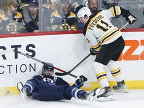 Winnipeg Jets forward Mark Scheifele (left) is tripped by Trent Frederic of the Boston Bruins during the first period in Winnipeg on March 16, 2023.