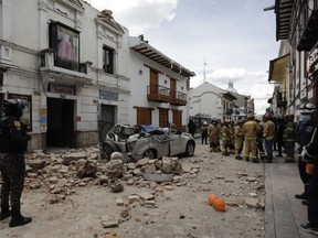 Rescue workers stand next to a car crushed by debris after an earthquake in Cuenca, Ecuador, Saturday, March 18, 2023.