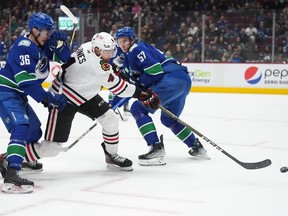 Chicago Blackhawks' Seth Jones takes a shot on goal as he skates between Vancouver Canucks' Akito Hirose and Tyler Myers during the first period of an NHL hockey game in Vancouver, on Thursday, April 6, 2023.