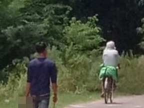 Man walking on road behind person on bicycle.
