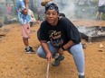 Woman holding stick, crouching by fire.