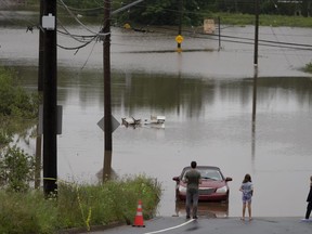 People stand at the edge of floodwater as vehicles are seen abandoned in water following a major rain event in Halifax on Saturday, July 22, 2023.