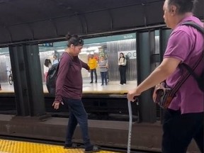 Woman pretending to tightrope-walk along TTC subway tracks edge.