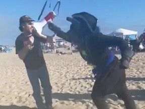 Man in black wolf costume, right, hits man filming group with megaphone.
