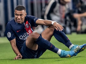 Paris Saint-Germain's French forward Kylian Mbappe grimaces as he sits on the pitch.