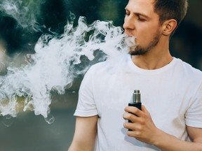 Young man with a beard vaping, blowing a lot of smoke
