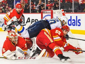 CALGARY, CANADA - OCTOBER 26: Brayden Schenn #10 of the St Louis Blues crashes into Jacob Markstrom #25 (L) and Noah Hanifin #55 of the Calgary Flames during the second period of an NHL game at Scotiabank Saddledome on October 26, 2023 in Calgary, Alberta, Canada.